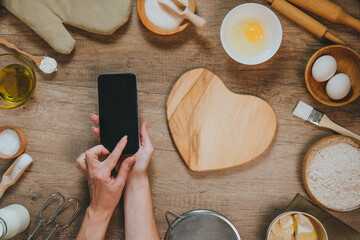 Female hands using smartphone with epmty screen near heart shape wooden board