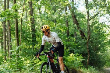 Fototapeta na wymiar Male cyclist rides a bicycle in a green summer forest, looks ahead, wears professional equipment.