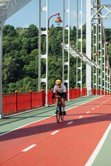 Photo of a professional cyclist training on a sunny summer day, riding on the bridge. Vertical.