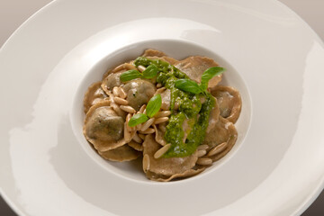 Round ravioli (tortelli) of wholemeal flour with pine nuts and Genoese pesto and basil leaves in white dish, close up