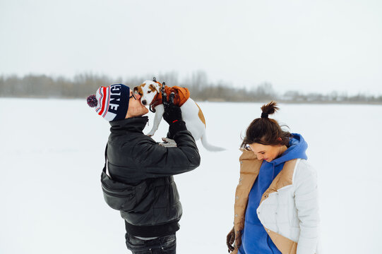 Happy young couple on a walk with a pet on a frozen snow-covered lake. Man and a woman are walking a Jack Russell dog