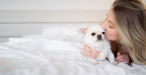 Beauty caucasian woman in pajamas in bed and kissing her cute little brown chihuahua dog Sleeping rest alone on the bed. Banner.