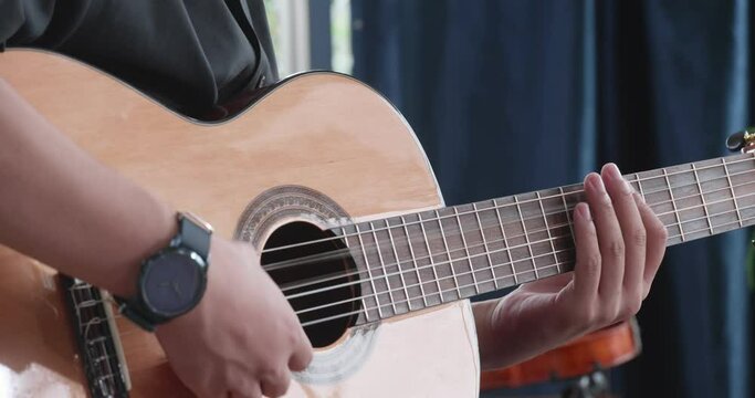 Asian man hands tuning acoustic guitar strings before playing music at home
