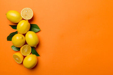 Many fresh ripe lemons with green leaves on colored background, top view, space for text