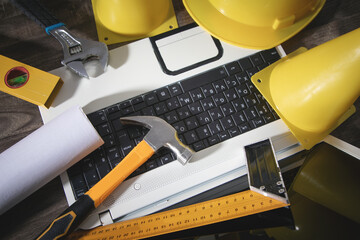 Yellow traffic cone, helmet, document, hammer, wrench with a laptop. Under construction