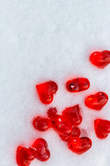 Set of small bright red glass hearts on powdery snow of snowdrift at cold winter day, symbol of romantic love, St. Valentine's Day holiday concept, top view placer vertikal image witth copy space