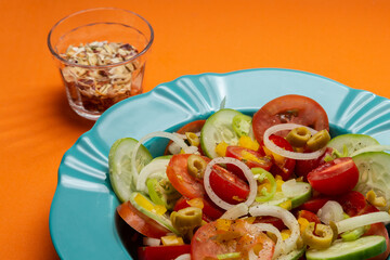 Um prato com salada de vegetais e um vidro com temperos desidratados sobre um fundo alaranjado.