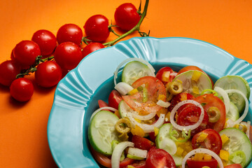 Um prato com salada de vegetais e um cacho de tomates, sobre fundo de cor alaranjada.