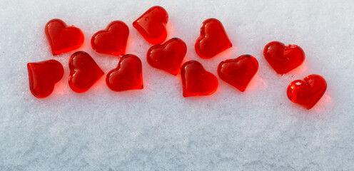 Set of small bright red glass hearts on powdery snow of snowdrift at cold winter day, symbol of romantic love, St. Valentine's Day holiday concept, top view placer banner