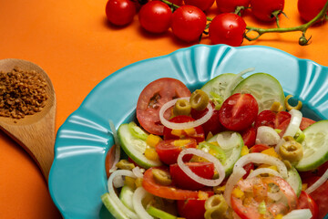 Um prato com salada de vegetais, uma colher com tempero desidratado e um cacho de tomates, sobre fundo de cor alaranjada.