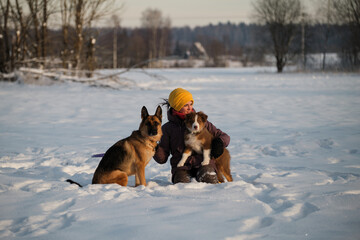 Spend time outside with pets. German and Australian Shepherd. Aussie puppy of chocolate color. Happy European girl on walk in winter park with two purebred dogs is sitting in snow.