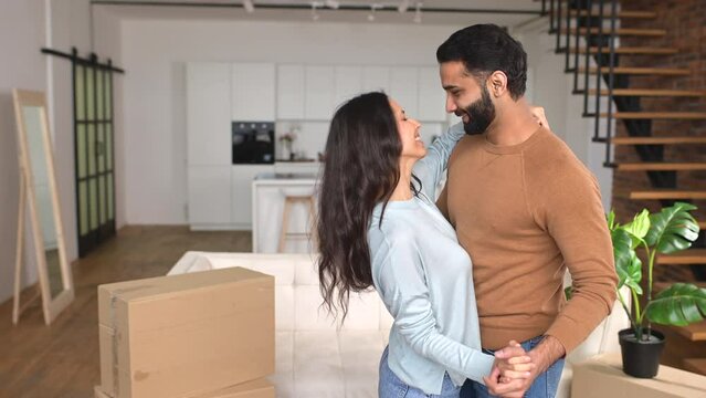Handsome man and attractive young woman is celebrating relocation, having fun together and dancing among cartboard boxes. Romantic interracial couple is rejoicing in new flat