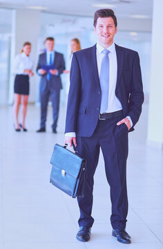 Portrait of young businessman in office with colleagues in the background