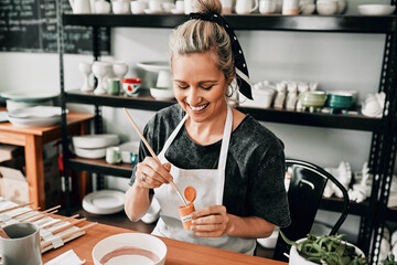 I love this colour. Cropped shot of an attractive mature woman sitting alone and painting a pottery bowl in her studio.