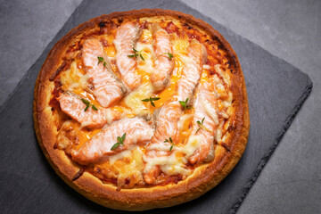 Delicious gourmet pizza with salmon on board with black table background. Homemade delicious pizza. Top view and copy space.