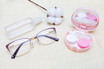 Glasses, cotton, and travel kit for contact lenses on background of a beige towel. Choosing between glasses and lenses. Caring for vision health. Poor vision concept.