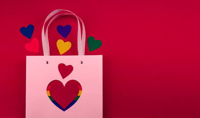 A pink gift bag on a red background with a heart and multi-colored