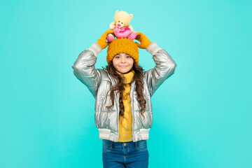 cheerful child in hat and puffer jacket with toy on blue background, gift