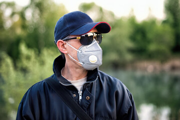 A man wearing respirator mask, sun glasses and a cap outdoors.