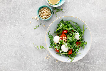 Fresh vegetable Caprese salad with arugula, tomato, pine nuts and mini mozzarella cheese. Top view