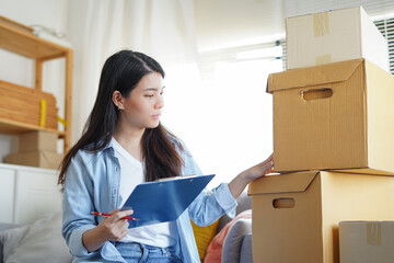 Asian woman checking and packing the carton box prepare to move to new house relocation shipping or...