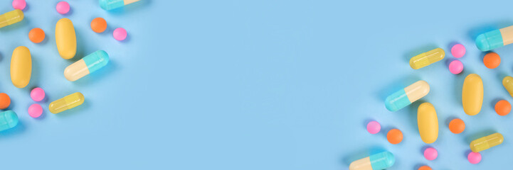 Banner made with assorted multicolored medicine pills, capsules and tablets on blue background with...