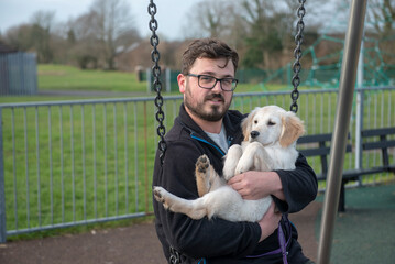 Caucasian man in thirties holding golden retriver puppy on a swing in the park