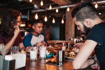 Multiracial friends eating breakfast in cafe. Young men chat while having tasty food and drinks. Guys hangout together