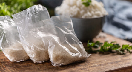 Raw rice in plastic bags on wooden background and cooked rice in bowl