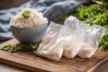 Raw rice in plastic bags on wooden background and cooked rice in bowl