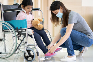 Fototapeta premium asian girl with a broken arm wearing a cast setting on wheelchair with her mother at hospital