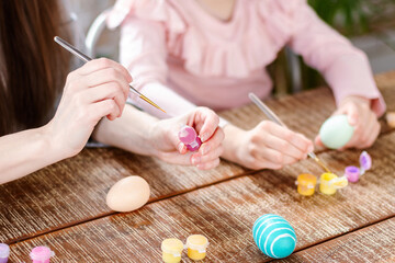 Happy Easter atmosphere! Close up funny, pretty, creative mom teacher, explain, to her cute, small, joyful daughter child how to draw, paint, decorate Easter eggs, together, sitting at desk