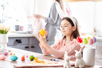 Obraz na płótnie Canvas Beautiful cute girl with bunny ears having fun draw, paint, decorate easter eggs. Working on kitchen desk with brushes and paint cartilage, smiling joyfully having fun. Celebrating spring holiday