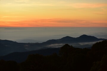 Obraz premium The sun set behind thick forests followed by mountains.