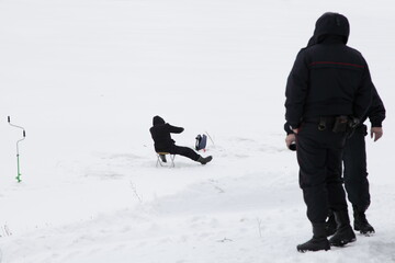Fototapeta na wymiar Winter fishing danger. One fisherman on ice and two watching policeman on shore
