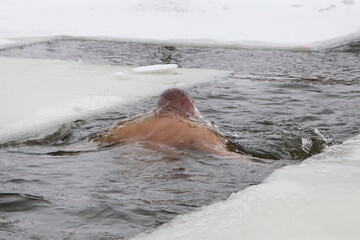 A believer swimm in cold water in an ice hole in the shape of a cross in winter outdoor. The...