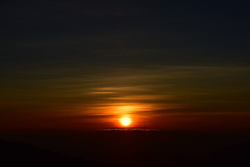 The sun set behind thick forests followed by mountains.