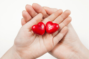 two red hearts lie on the palms of two hands on a white background isolated close-up