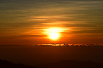 The sun set behind thick forests followed by mountains.