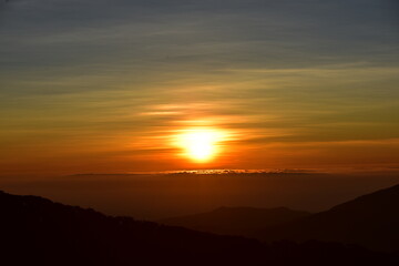 The sun set behind thick forests followed by mountains.