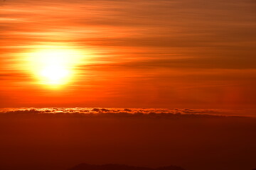 The sun set behind thick forests followed by mountains.
