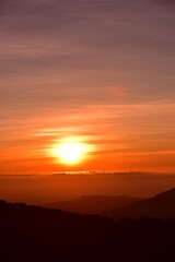 Obraz premium The sun set behind thick forests followed by mountains.