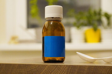 A bottle of medicine with a blue label and a measuring spoon stands on a wooden table