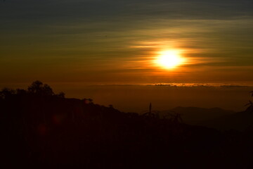 sunrisie or sun setting behind a dense forest area followed by mountains	