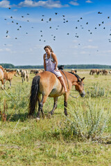 A young girl sits with her back on the horse backwards, birds fly in the distance.