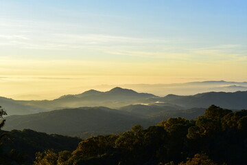 The sun set behind thick forests followed by mountains.