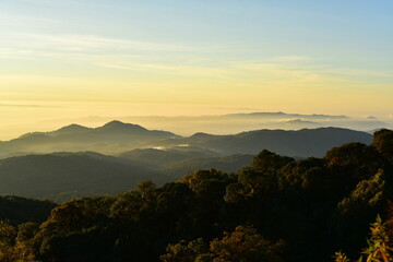 The sun set behind thick forests followed by mountains.