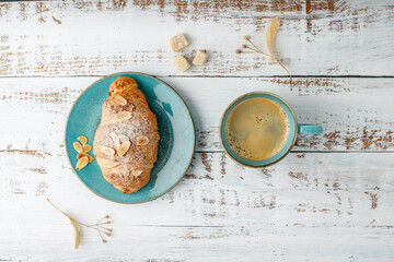 Fresh baked almond nuts breakfast croissant on vintage turquoise plate and hot coffee cup on rustic wooden background
