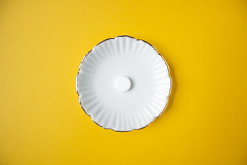 Dosed medication. Top view of white carved plate with only one round tablet on a yellow background. Space for text.