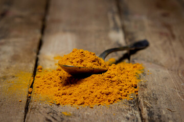Ground turmeric on a wooden background. A spoonful of turmeric is on the table. Traditional spices.